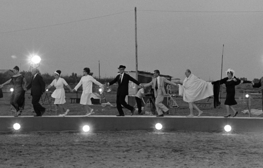 A group of people walking hand-in-hand on a narrow platform with lights below.