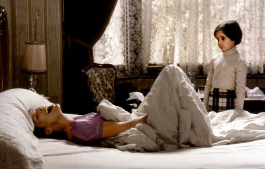 A woman is crying out in anguish laying on a bed while a younger child looks on.