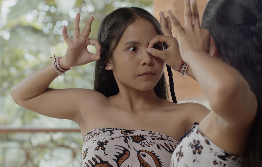 A woman with long hair and braids is dancing with her hands near her face. Her movements are being mirrored by another woman.