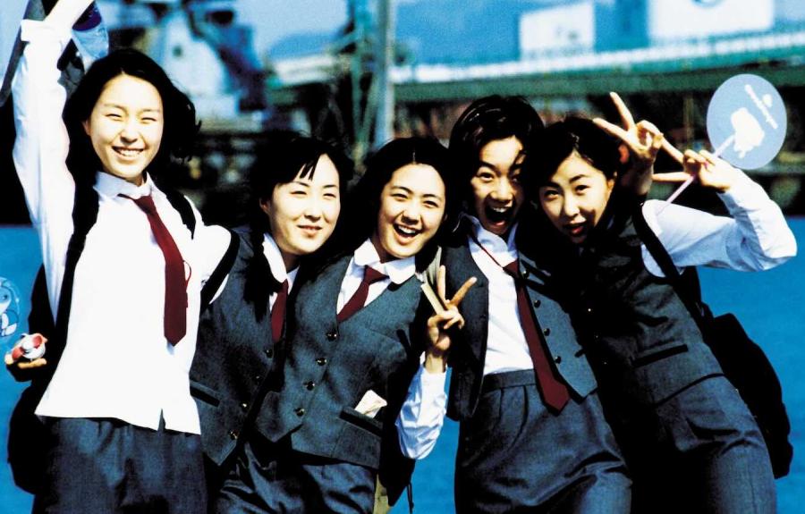 A joyful group of five girls posing in the school uniforms, which are charcoal gray with a white blouse and marron ties.
