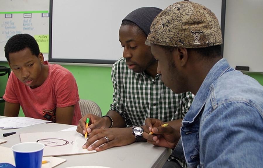 A teacher and two students are working together on a math problem in a classroom with a white board and green walls.