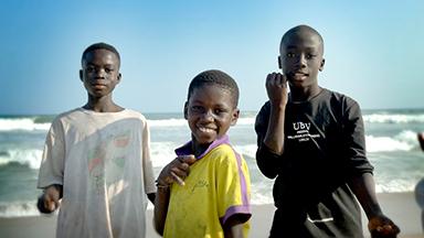 Three young men stand smiling and posing on a beach