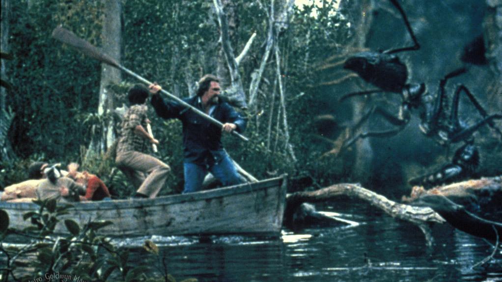 A man in a boat in swamp fights off a giant ant with an oar
