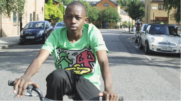 A young boy in a lime green shirt rides his bike down a city street.