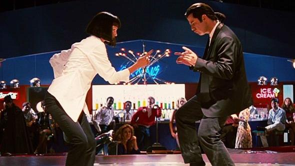 A woman in a white shirt and a man in a black suit dance the twist at the center of a night club/restaurant dance floor.