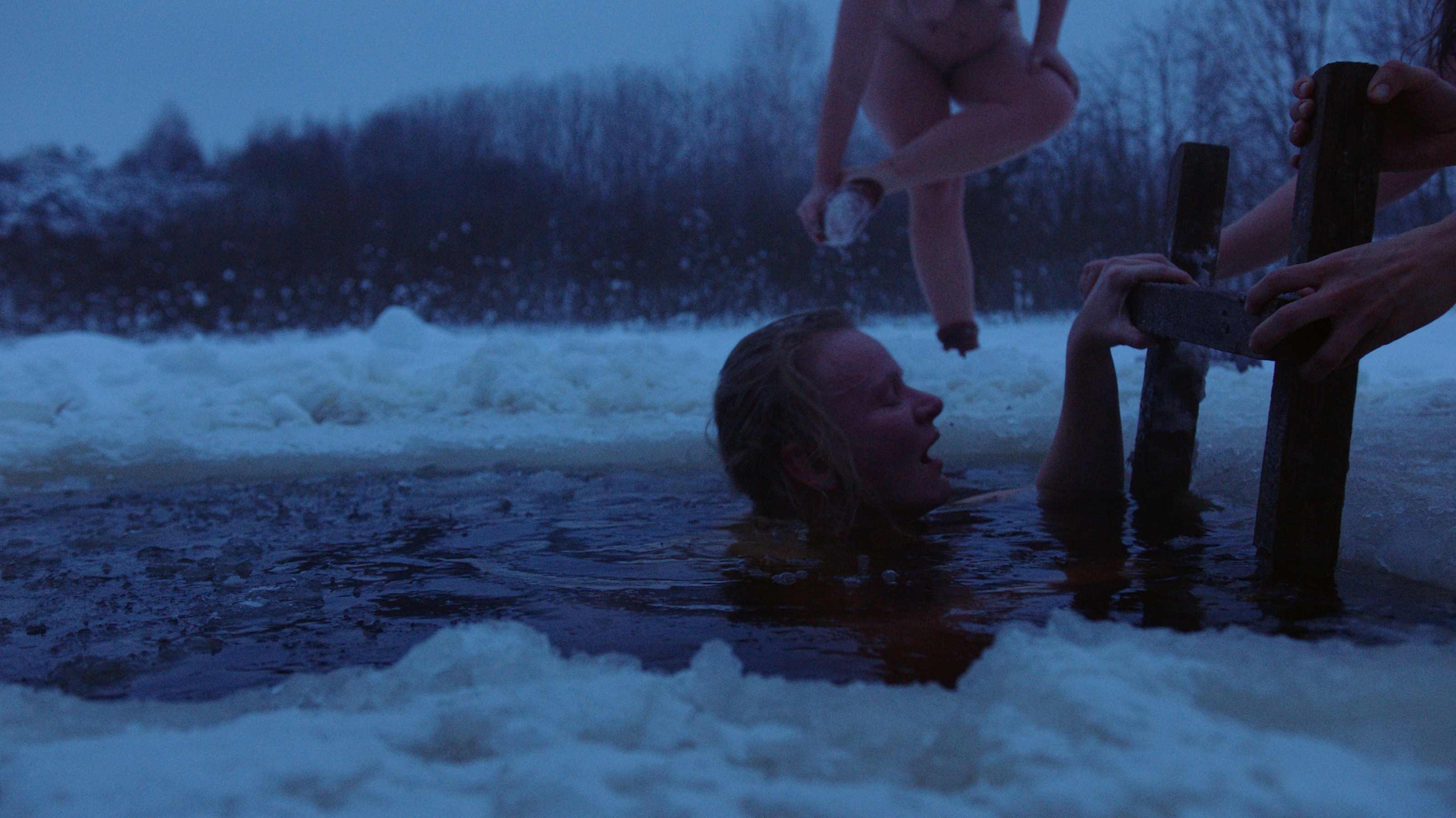 Nude women climbing out of water after swimming in snow-covered lake.