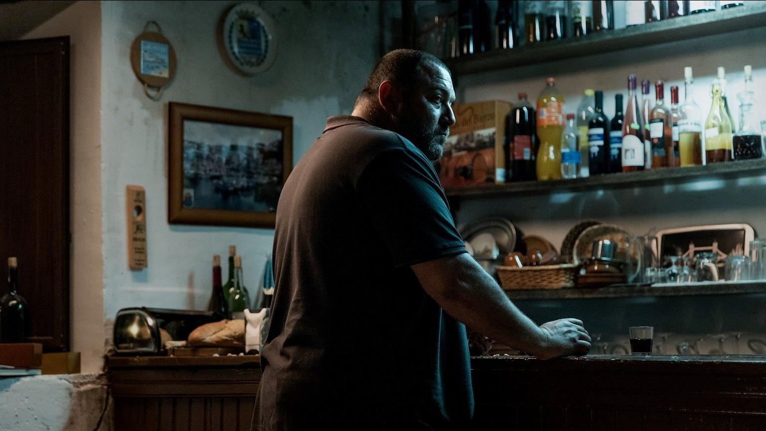 A man standing in a dimly lit kitchen leaning against the counter.