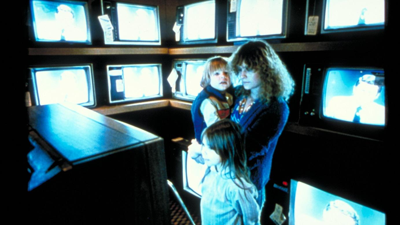 A woman and two children standing in a room filled with television screens.