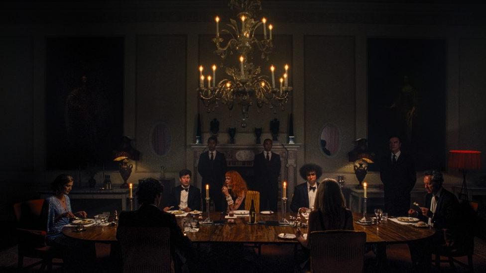 A group of people seated a a long dinner table beneath an elaborate chandelier.