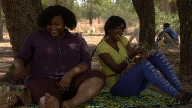 Two women sit laughing beneath a shady tree.