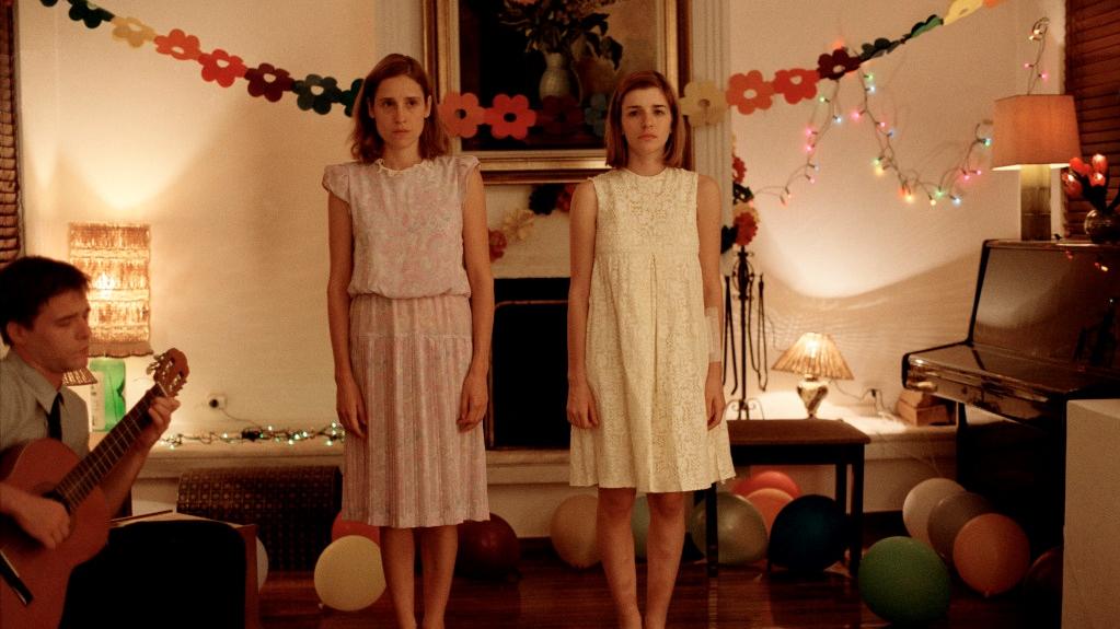 Two girls in dresses singing in a living room decorated for a party.