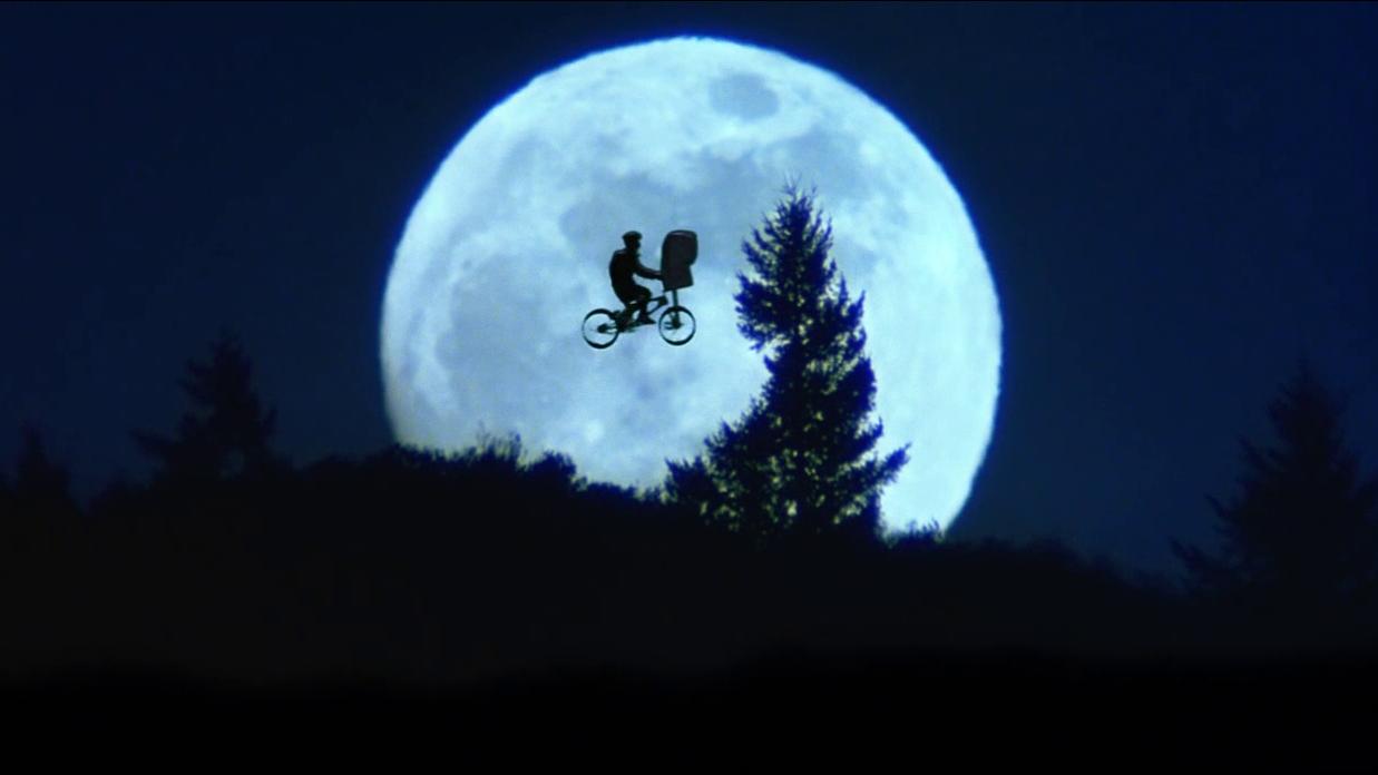 A silhouetted image of a boy riding a bicycle suspended in front of the moon.