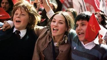 Three children in school uniforms cheering and waving flags.