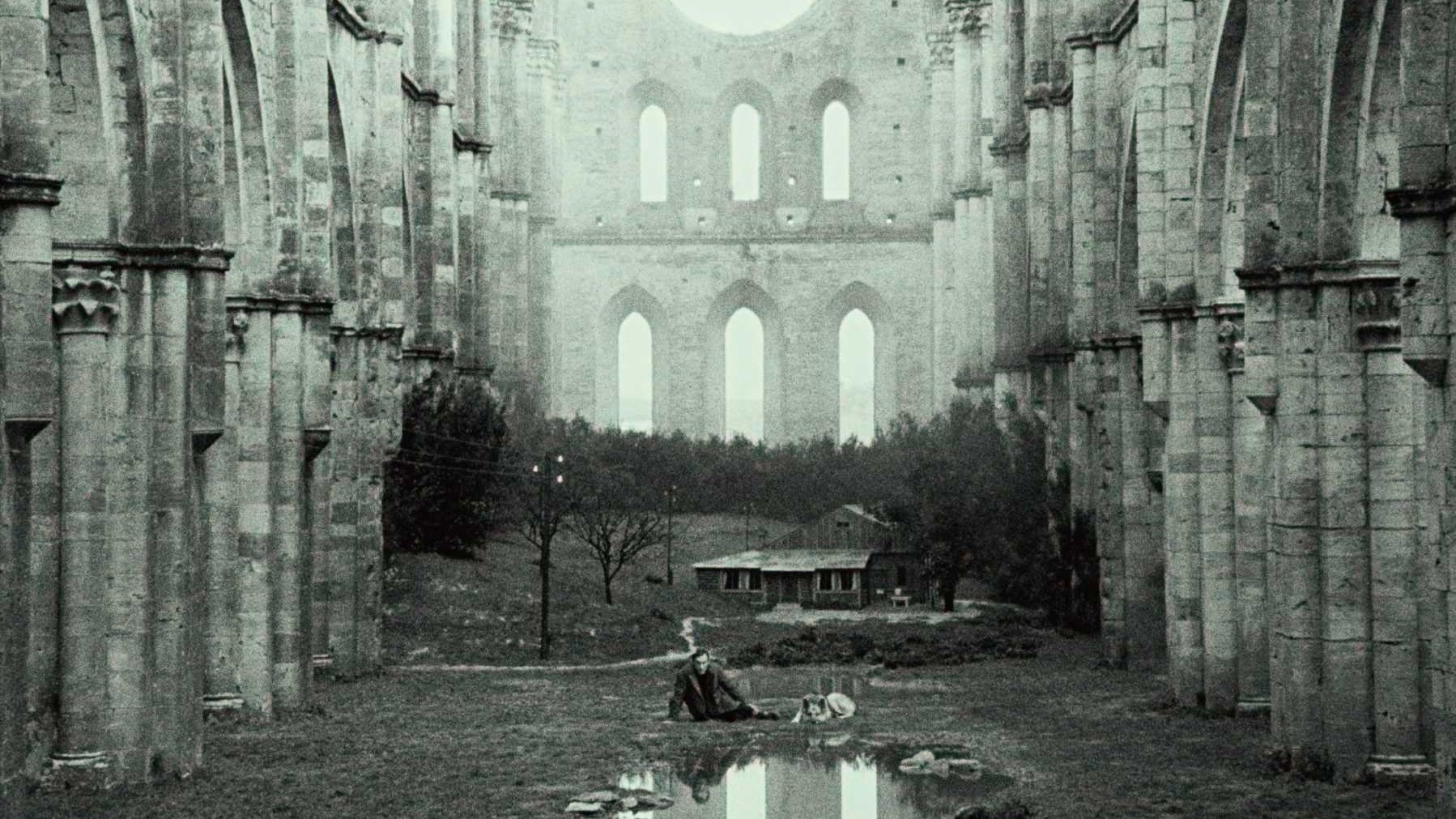 A black and white image of a man lying in the foggy ruins of a massive cathedral.