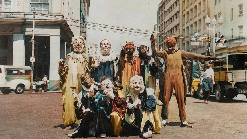 A group of people dressed in carnival-esque costumes standing in the middle of a city street.