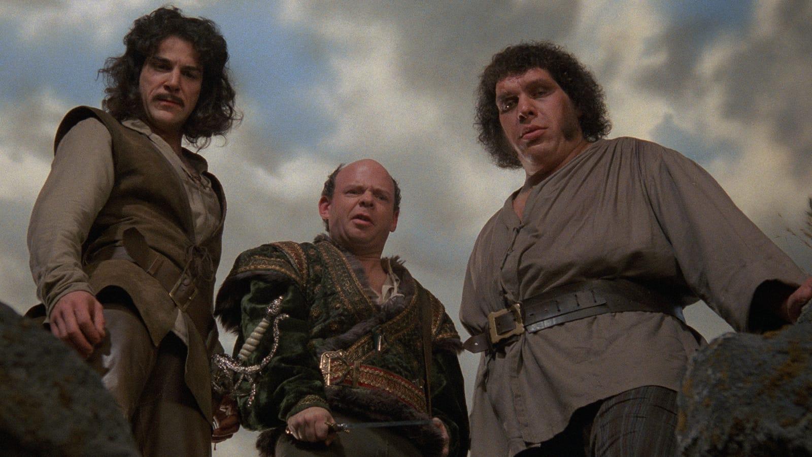 Three individuals standing outdoors with a cloudy sky in the background. They are dressed in costumes that suggest a historical or fantasy setting, with one character in the middle and the other two standing on either side.