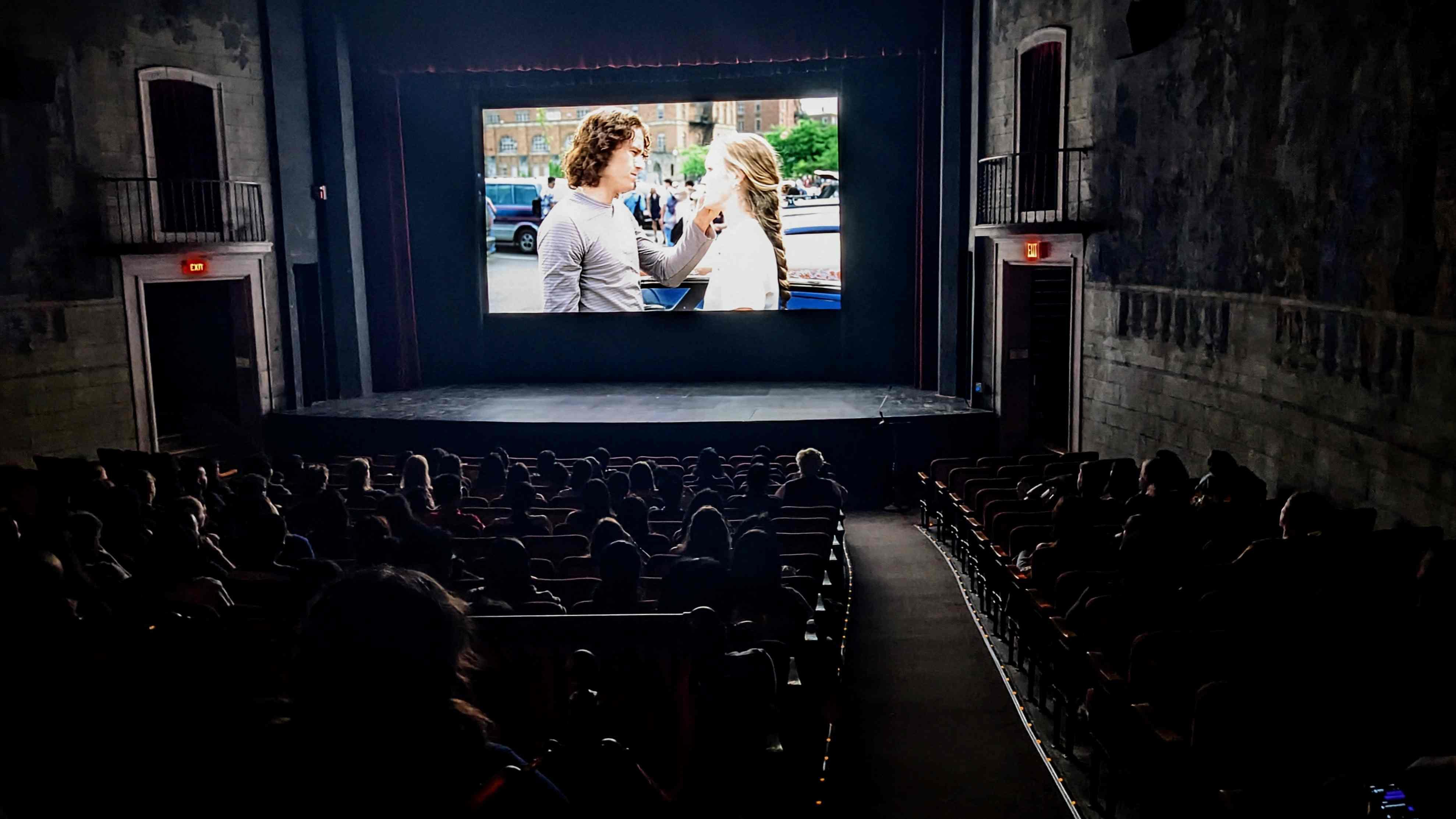 A crowded movie theater with a young couple on screen.