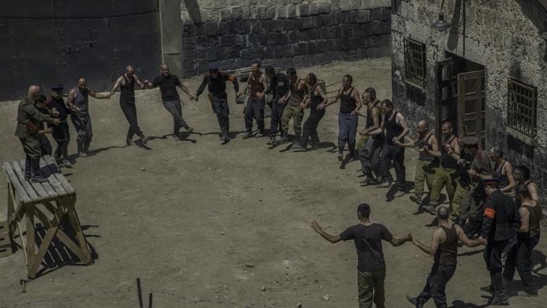 A group of man in a prison yard holding hands in a circle.