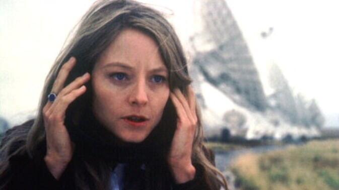 A close-up of a woman listening to headphones near massive satellites.