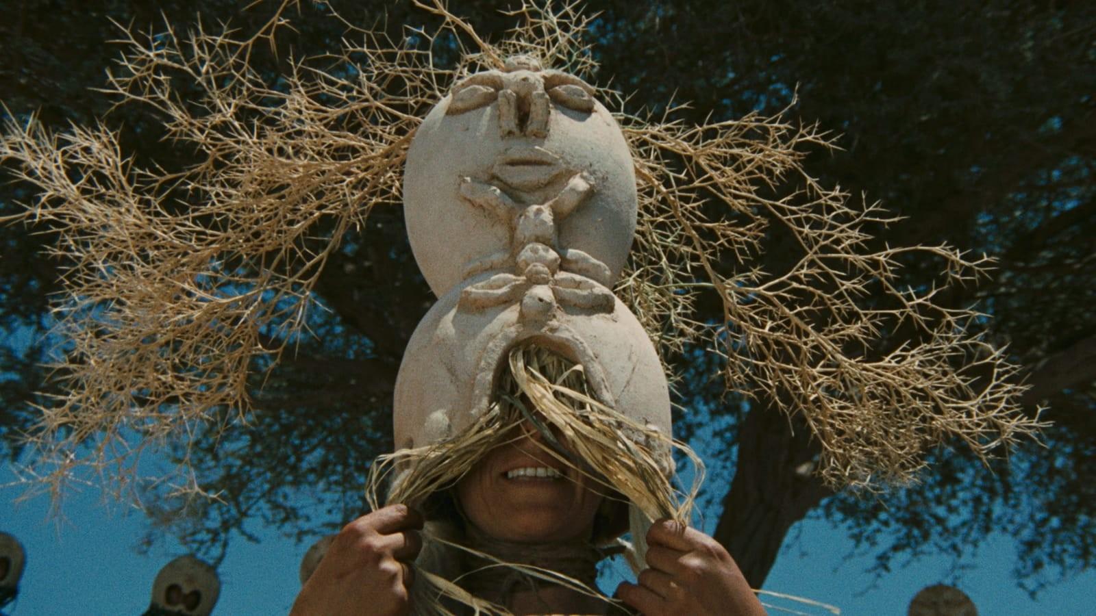 A man wearing a pagan headdress with sticks sticking out of the top.