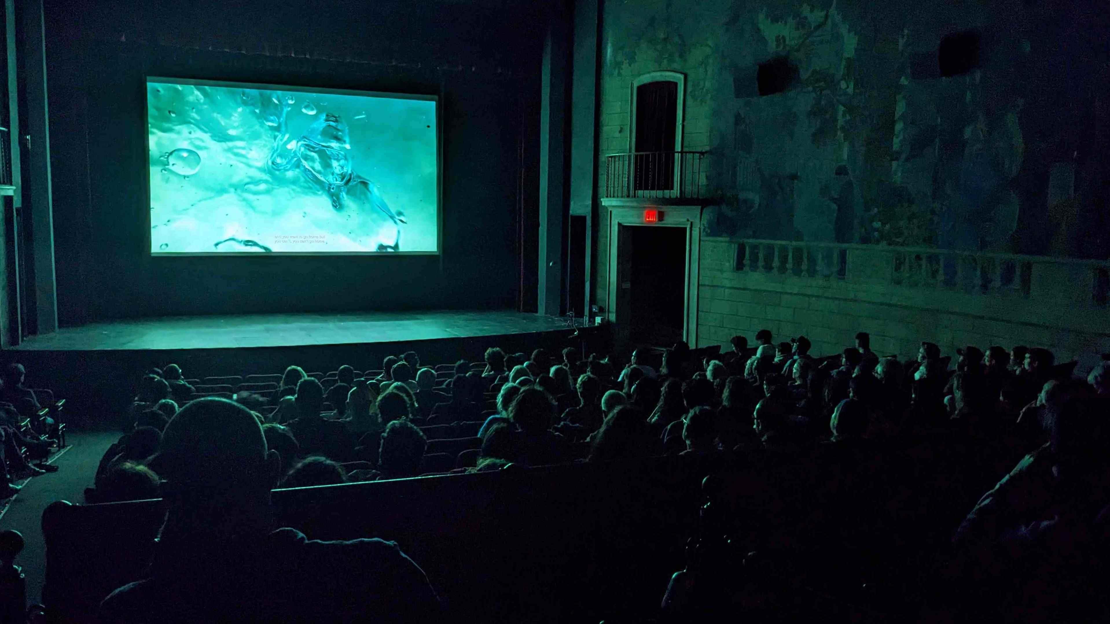 A crowded movie theatre with an image of water on screen.