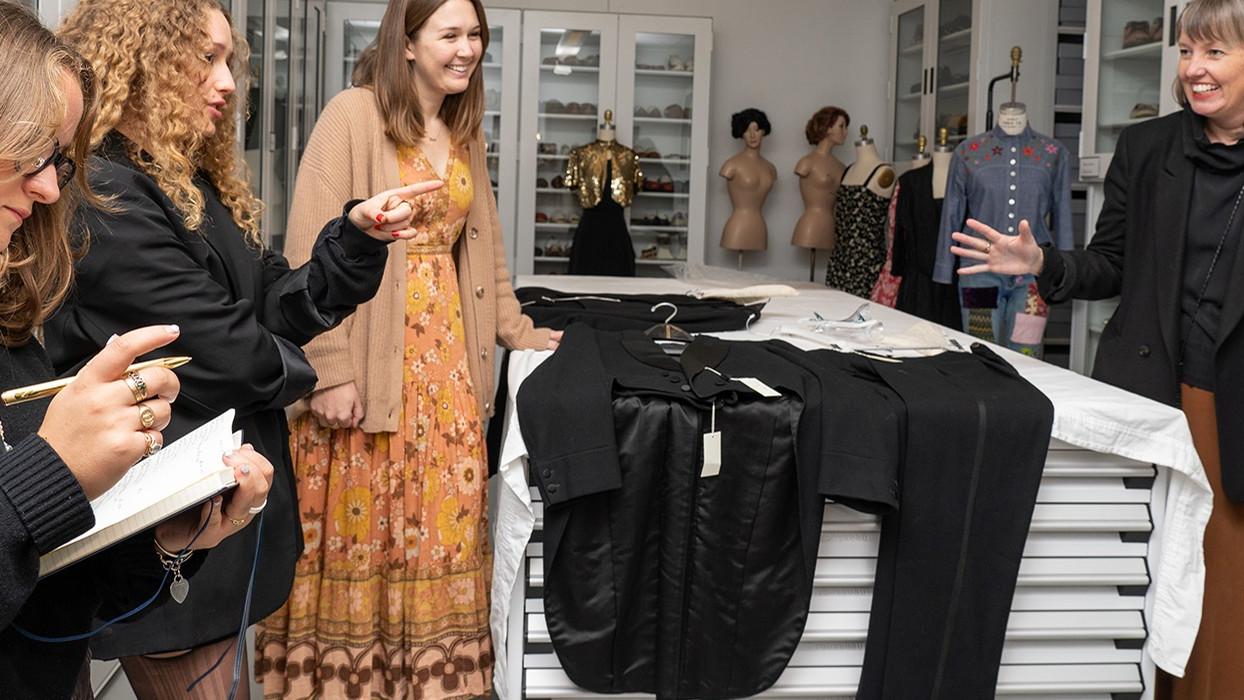 Four women standing together looking at a black tuxedo and laughing.