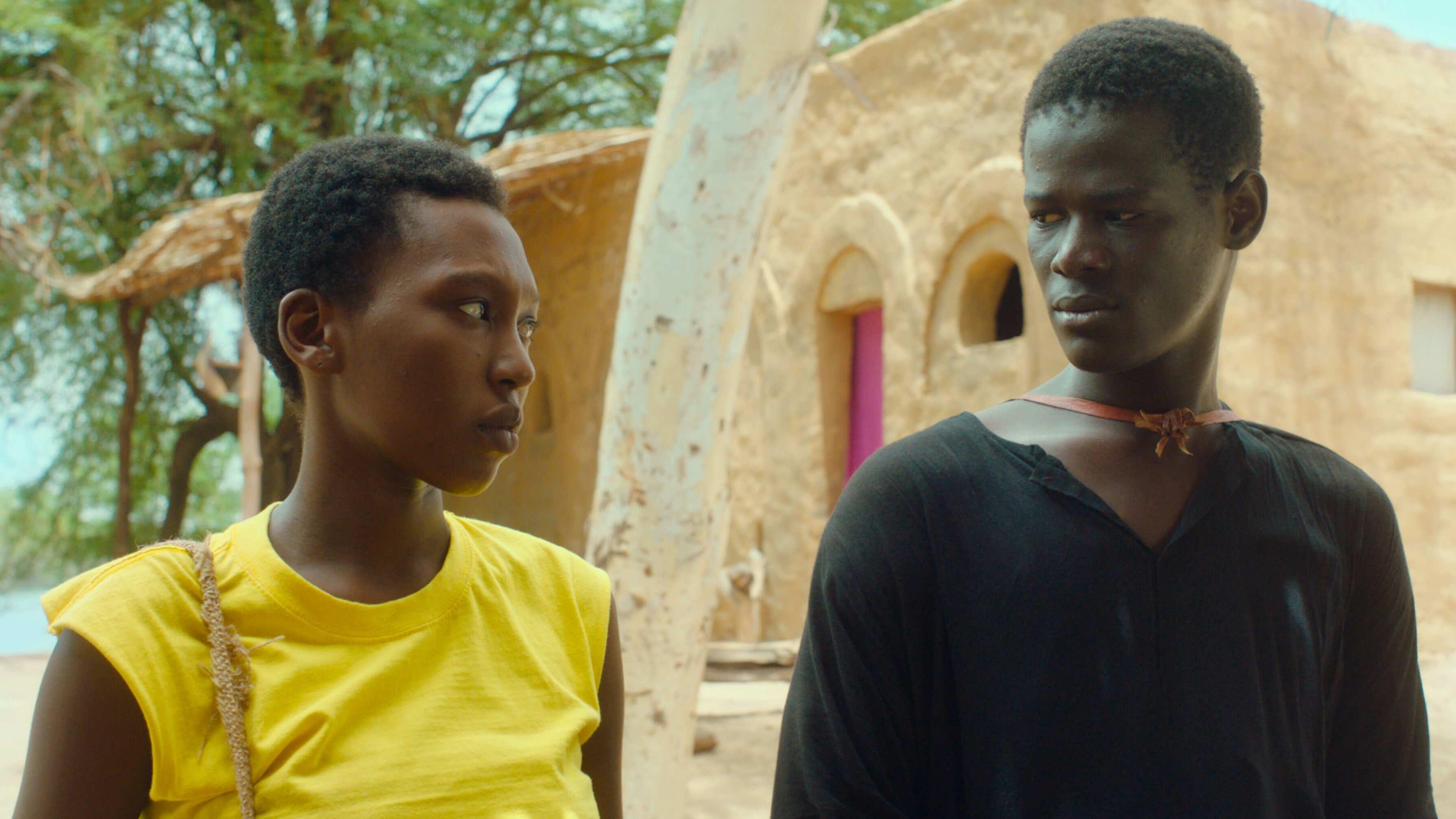 A young woman in a yellow t-shirt makes eye contact with a young man in a black t-shirt.