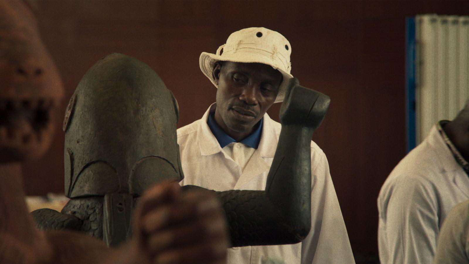 A man wearing a bucket hat and observing a statue of a warrior with its arm raised.