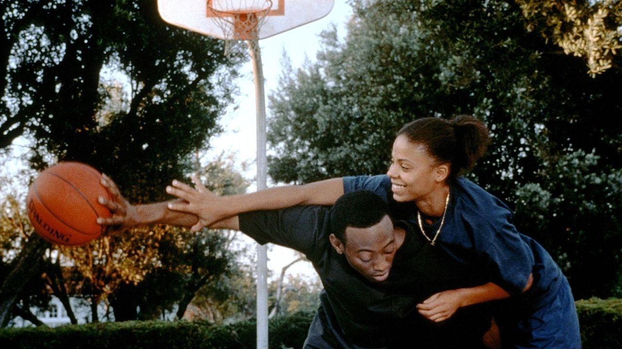 A smiling man and woman embrace while playing basketball.