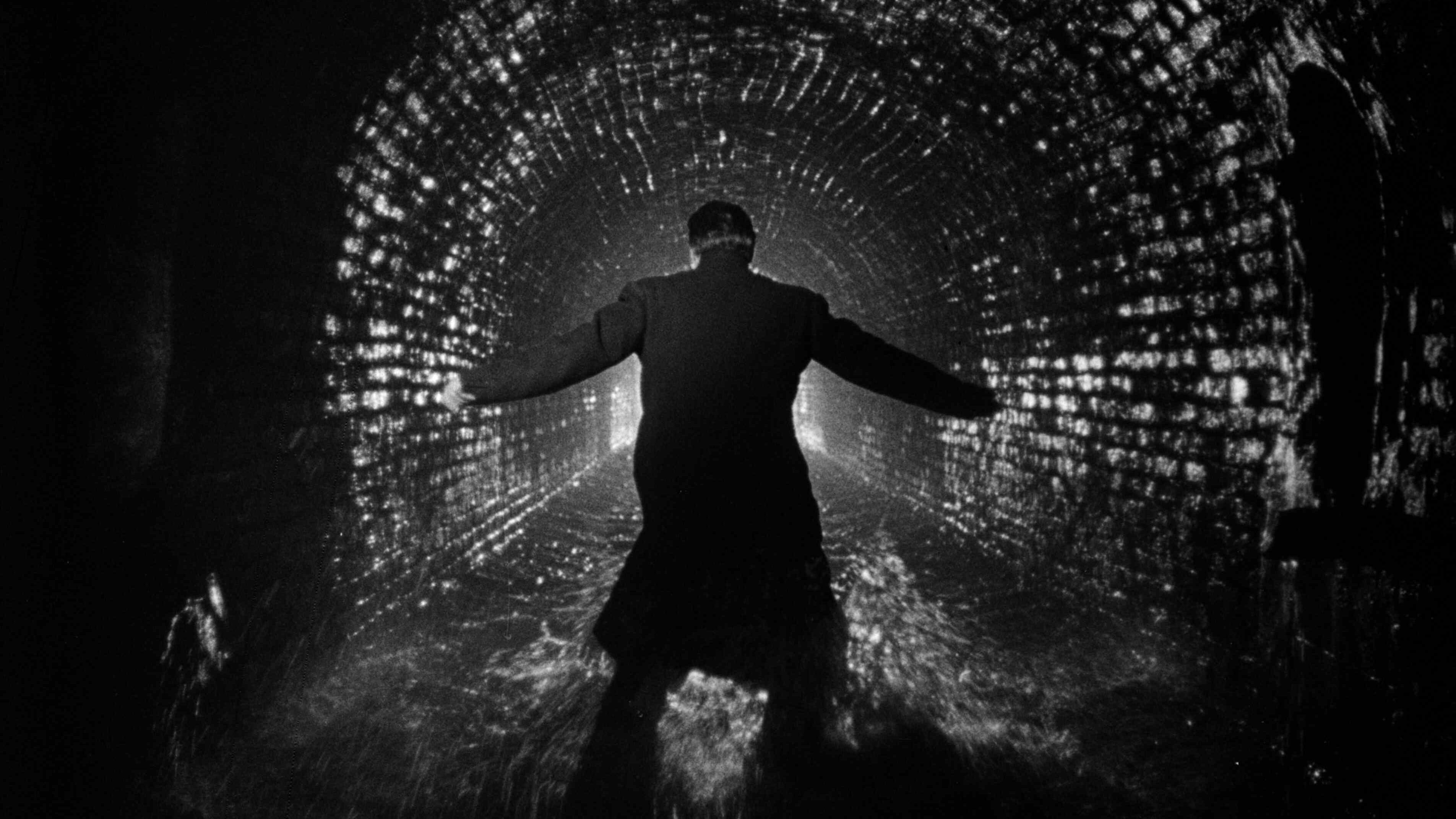 A monochrome image of a man running inside a dark tunnel with brick walls.