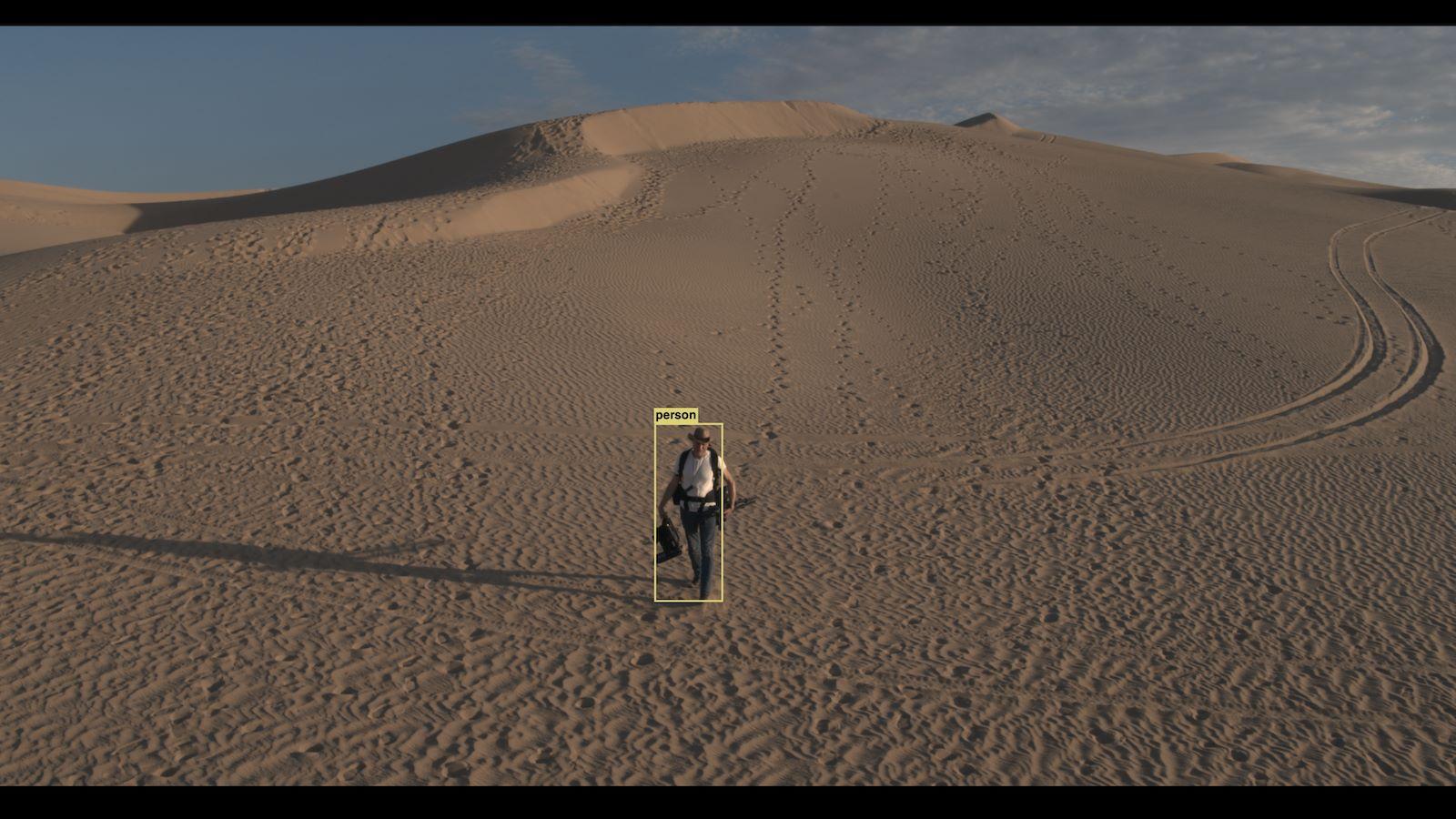 Photo of a man walking in sand dunes with a computer generated box drawn around him.