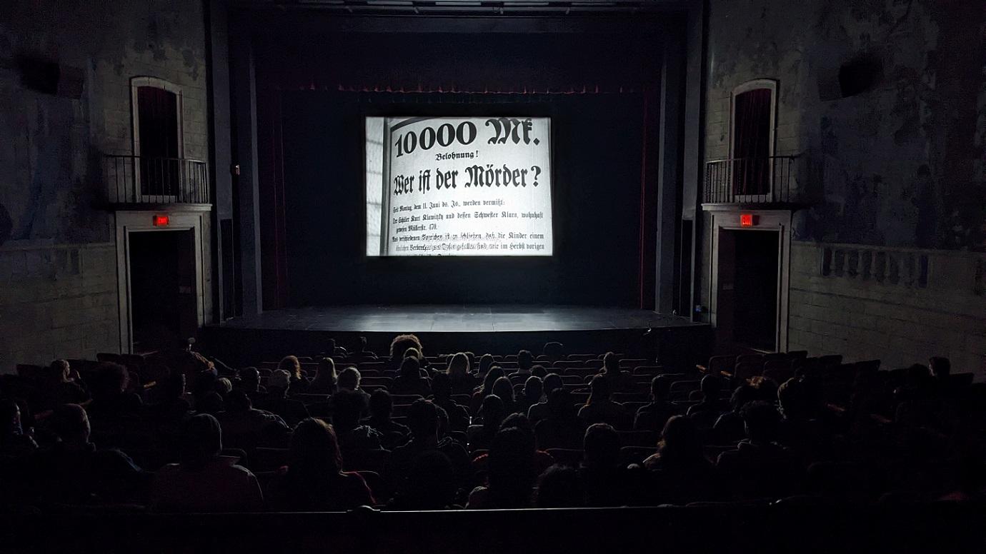 A group of people watching an old movie inside a darkened theatre.