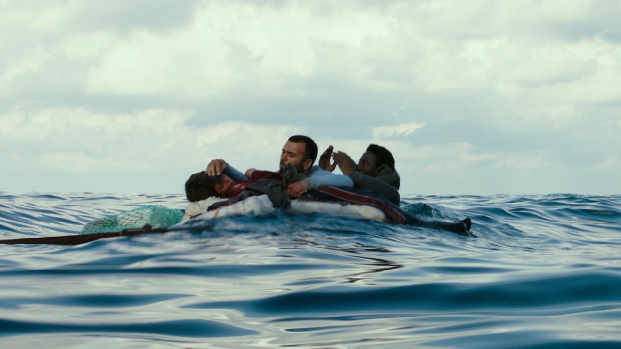 A man and two children cling to a raft in the middle of the ocean.