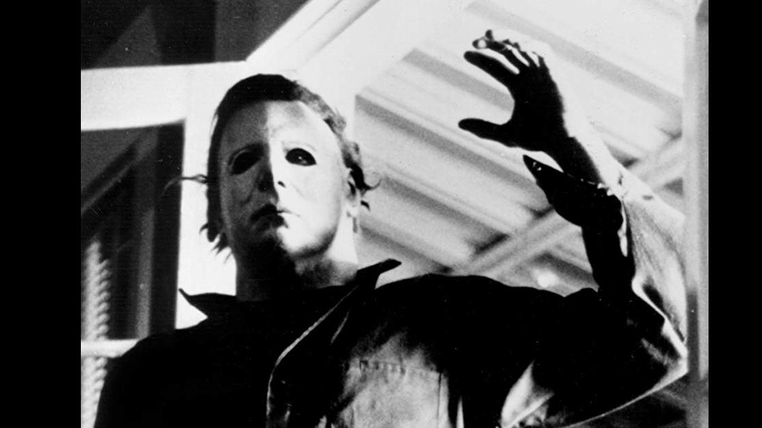 A black and white photo of a masked man with his arm raised.