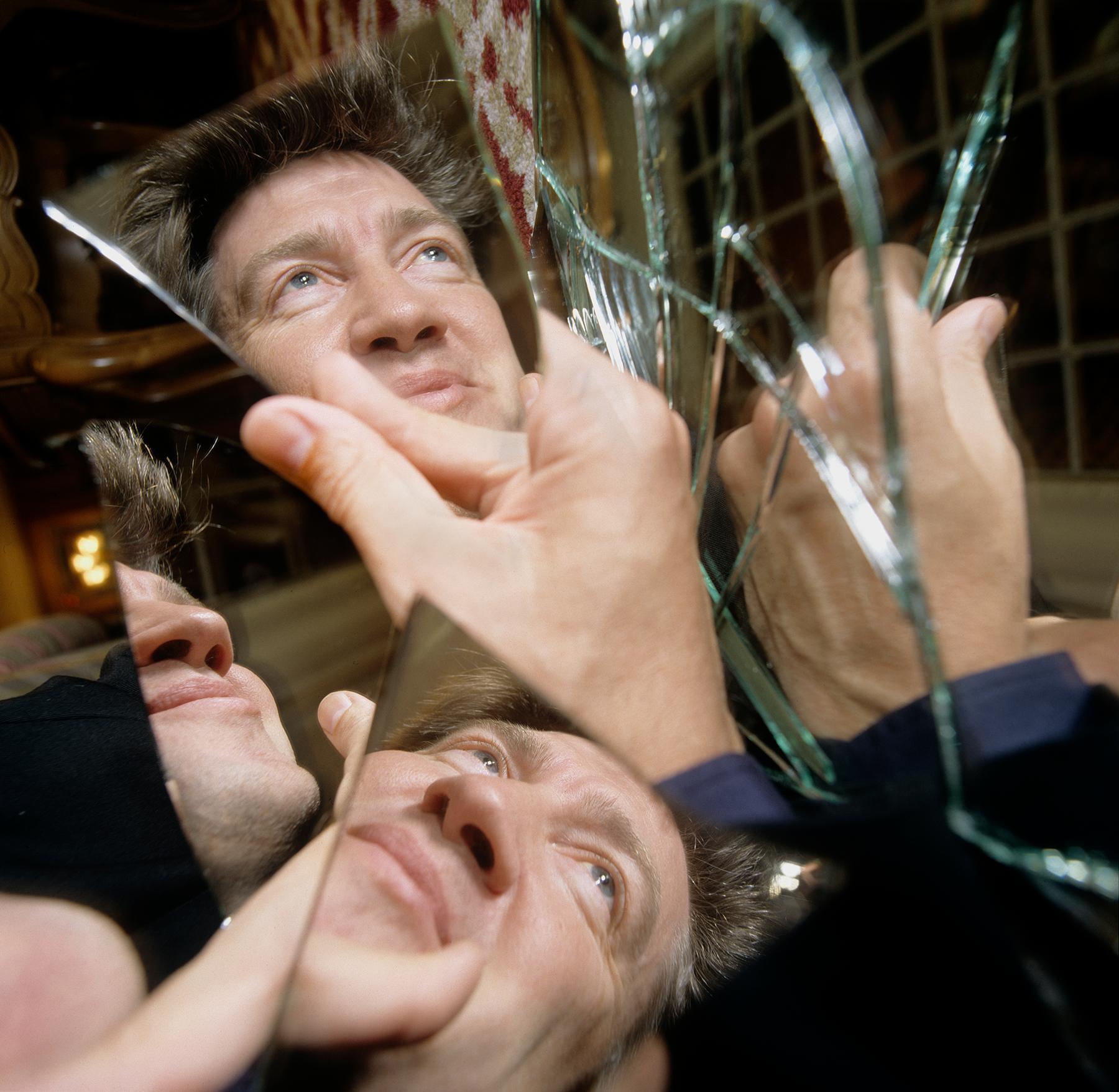A person holds a broken mirror, with reflections of their face and hands visible in the shards