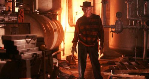 A man with a distorted face wearing a hat and gloved hand with knives attached, stands in front of an industrial background