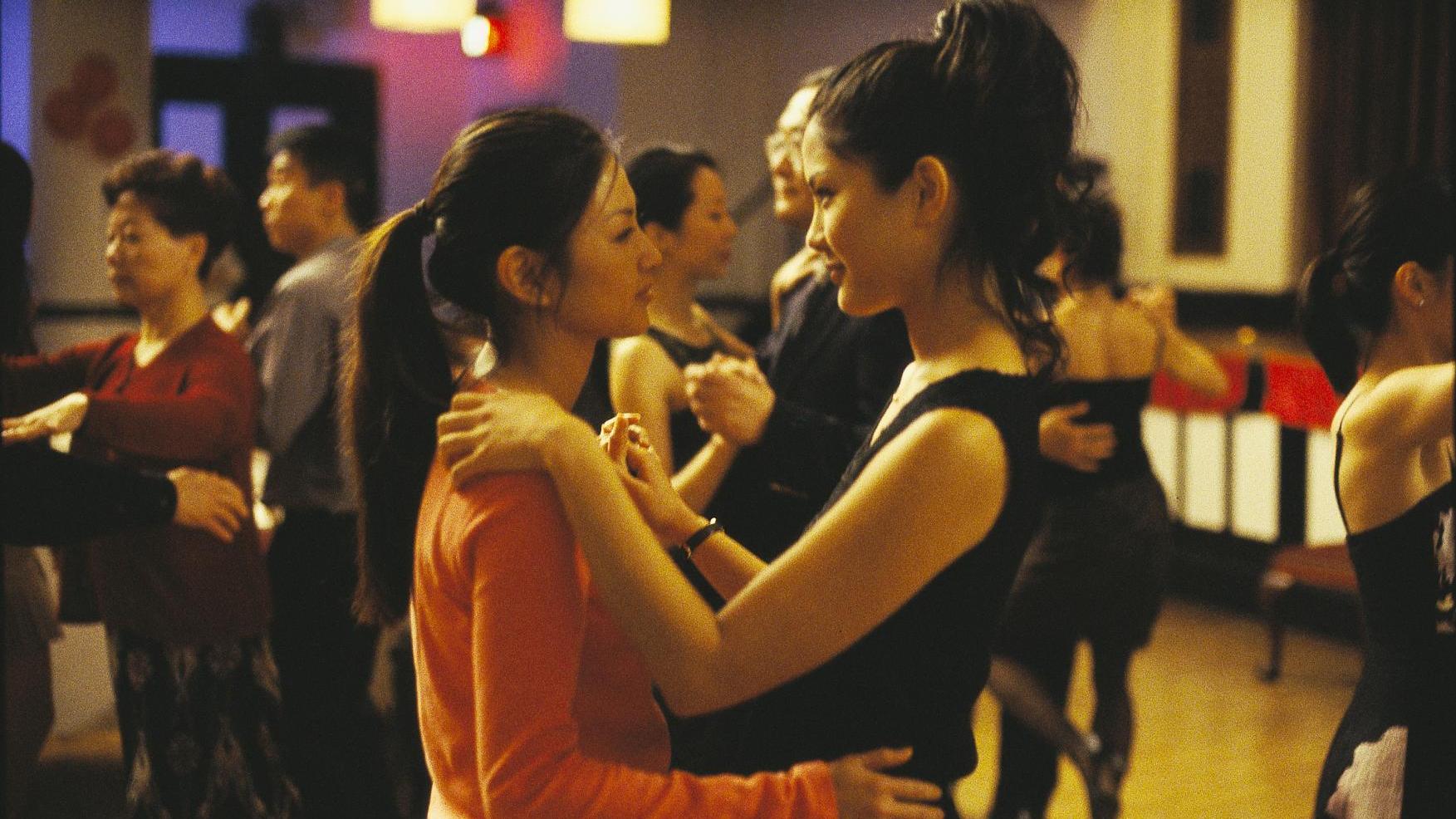 Two women dancing closely at a social event, with other dancers in the background