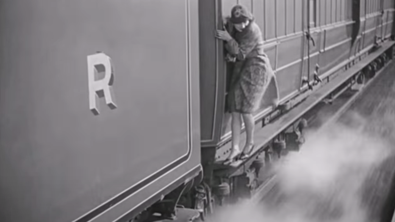 A well dressed woman clings to the side of a moving freight train.