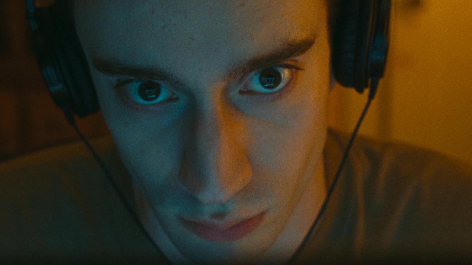 A close up image of a man wearing headphones and staring ahead intensively with a vacant expression.