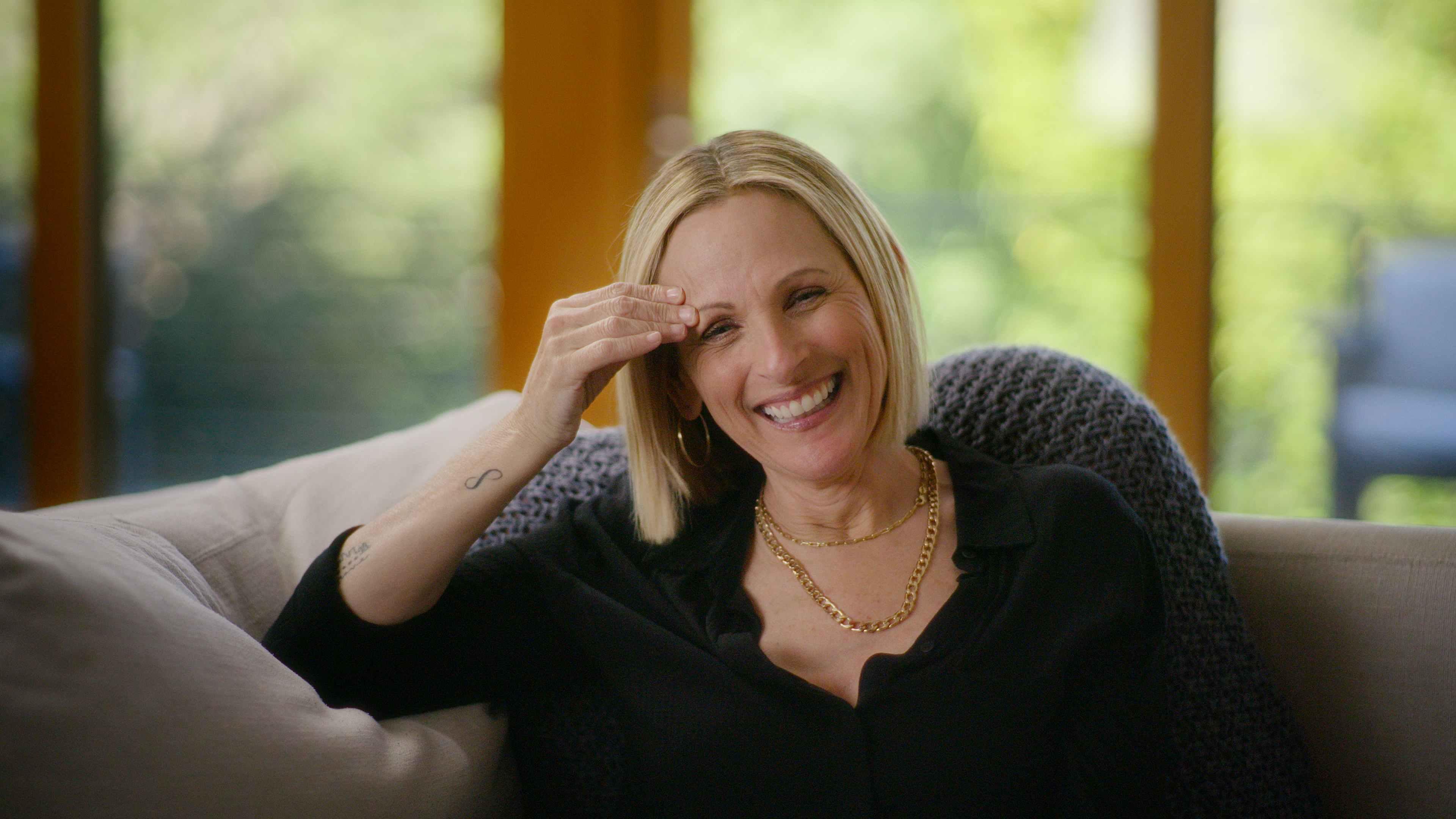 A woman with short blonde hair is laughing with one had touching her forehead.