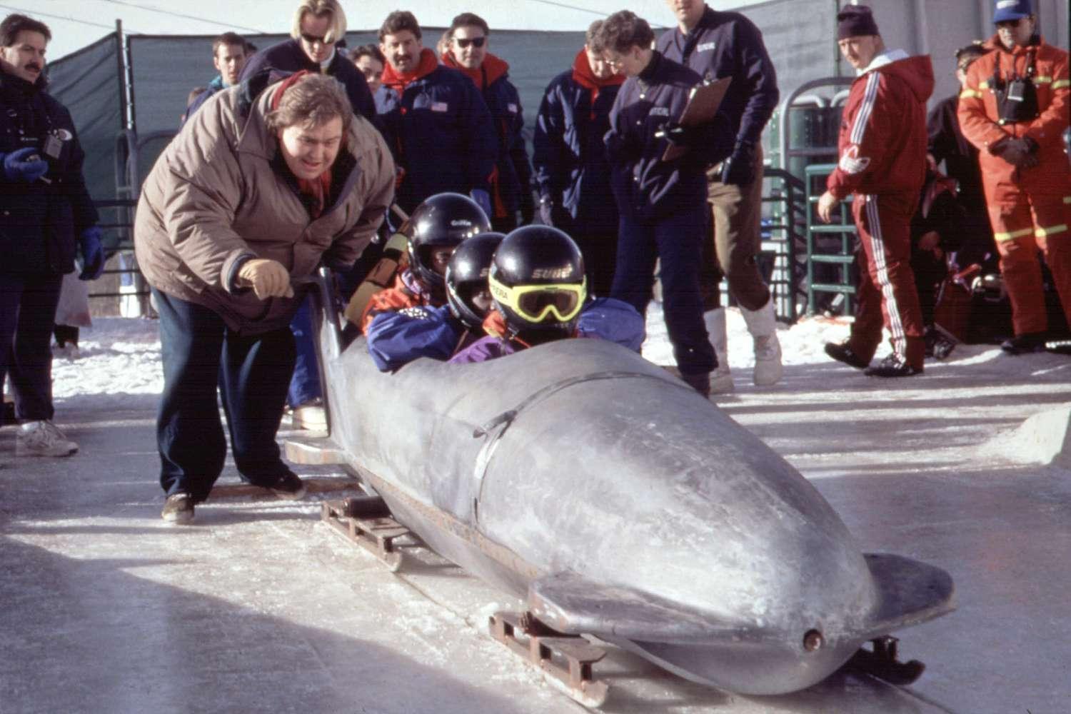 A bobsled team prepares for a run on a snowy track as a coach leans in to speak with them.