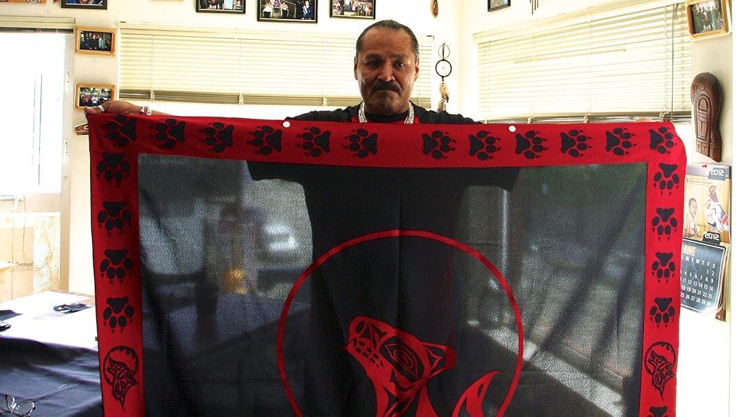 A person holds up a black cloth with red border featuring paw prints, skulls, and a stylized animal head.