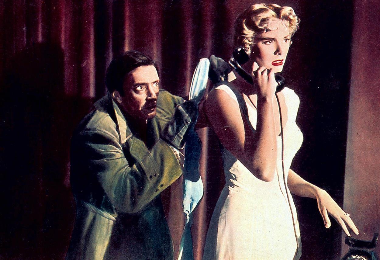 A woman in a white dress holds a black rotary phone to her ear as a man in a green coat reaches toward her with a cloth. The dark red curtains and dramatic lighting heighten the suspense of the moment.