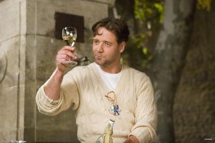 A man in a cable-knit sweater holds up a glass of white wine outdoors near a stone structure.