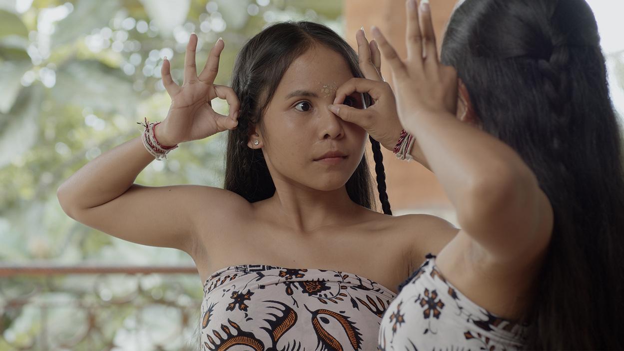 A woman with long hair and braids is dancing with her hands near her face. Her movements are being mirrored by another woman.