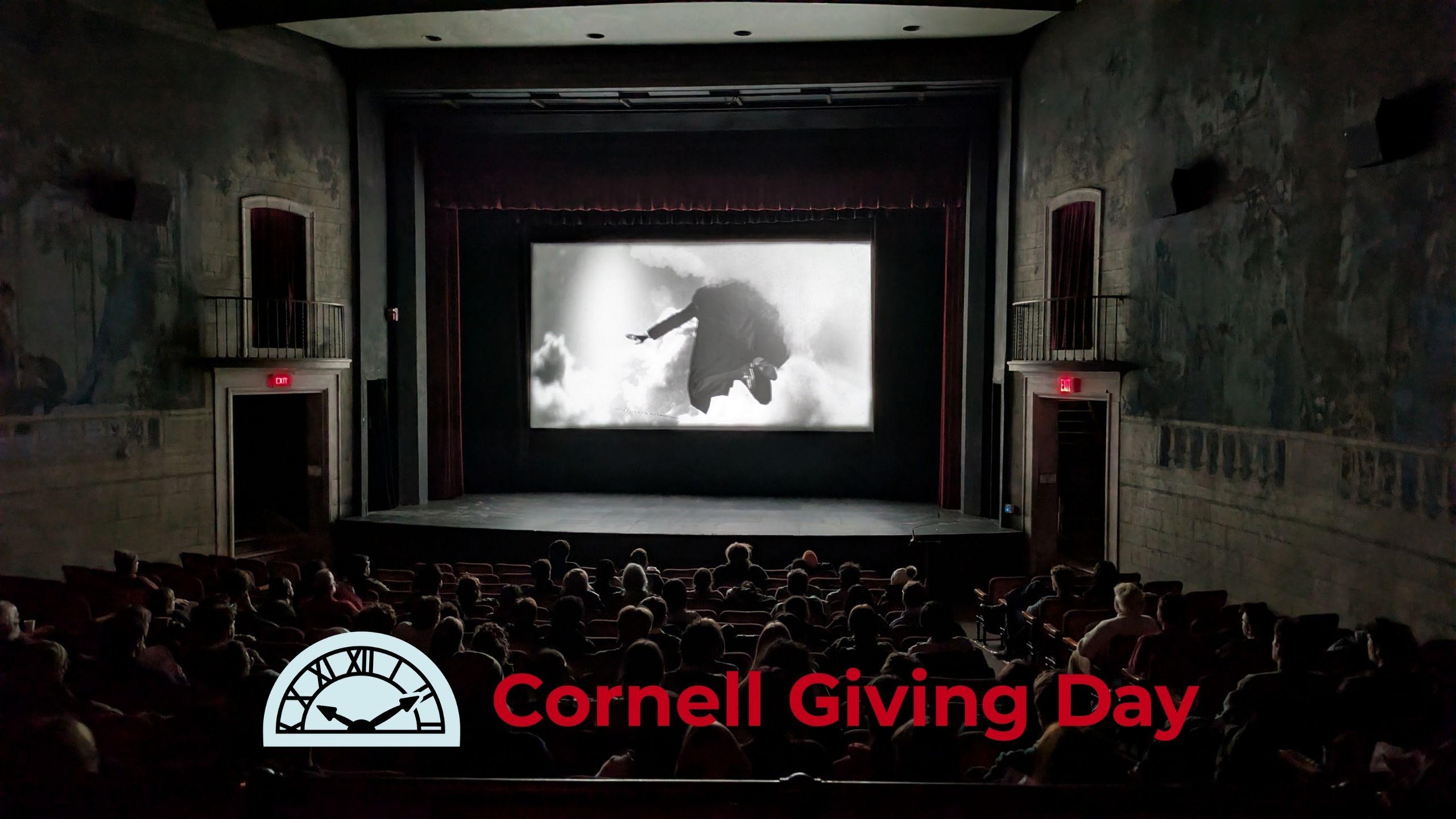 A group of people inside a darkened movie theatre with an image of a man flying through clouds on screen.