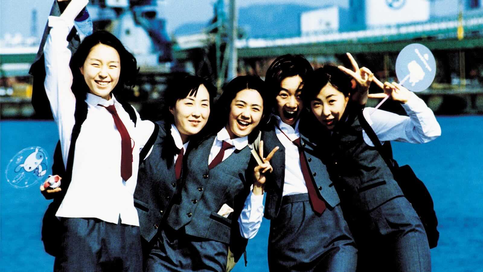 A joyful group of five girls posing in the school uniforms, which are charcoal gray with a white blouse and marron ties.