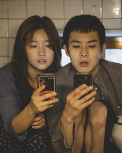 A girl and a boy sit very close together looking at their phones.